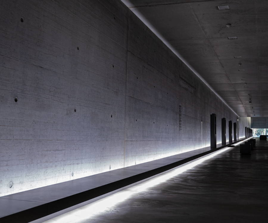 Beleuchtete Betonwand im Inneren der Gedenkstätte Bergen-Belsen in grauen Farbtönen