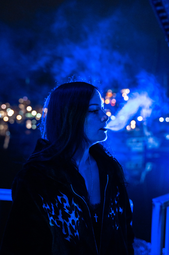 Karina Rose pustet Rauch aus, seitlich zur Kamera im blauen Licht