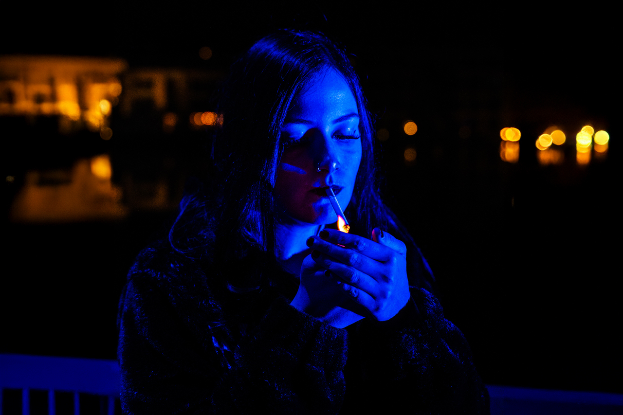 Karina Rose im blauen Licht zündet eine Zigarette an, Feuer im Kontrast