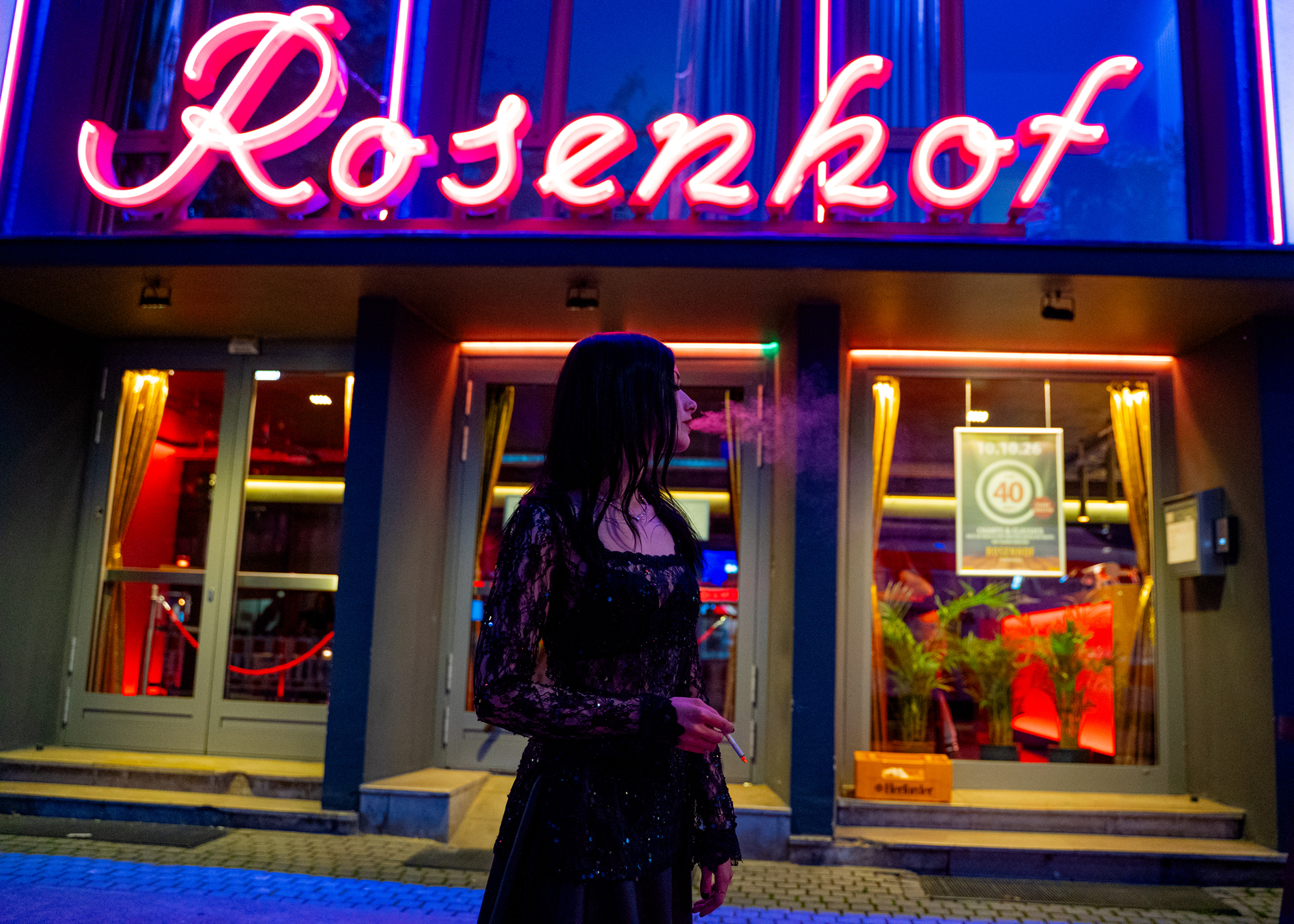 Karina Porträt vor dem Rosenhof Neon Schriftzug, Zigarette in Hand und Rauch auspustend