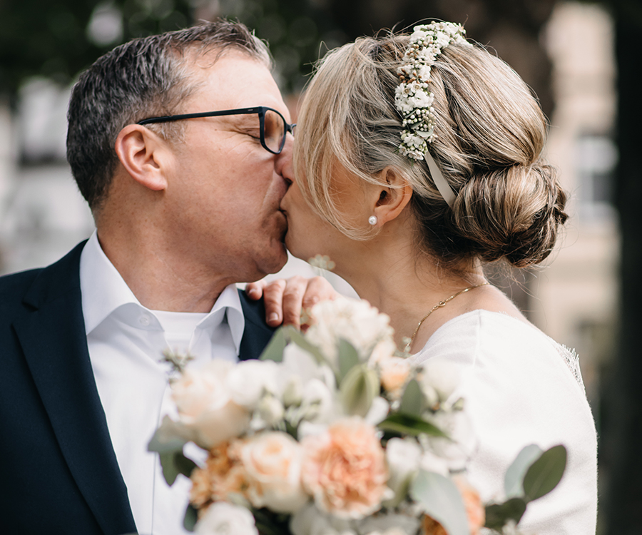 Brautpaar küsst sich, die Braut hält einen Blumenstrauß