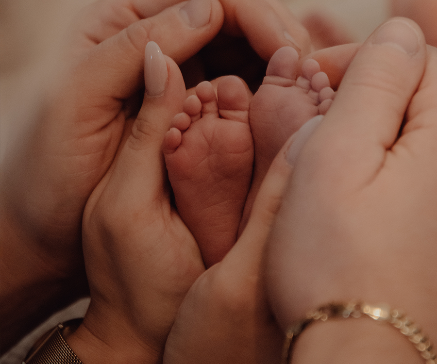 Zwei erwachsene Hände halten die Füße eines Babys