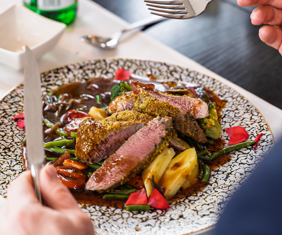Scharf gewürztes Lammfilet in Pistazienkruste mit gegrilltem Gemüse, Foodfoto mit unscharfer Person im Hintergrund